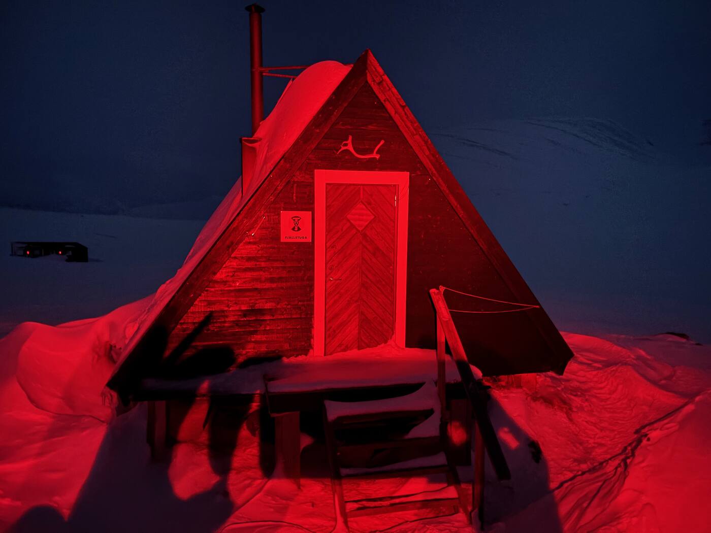 Petite fjällstuga triangulaire éclairée en rouge dans la neige